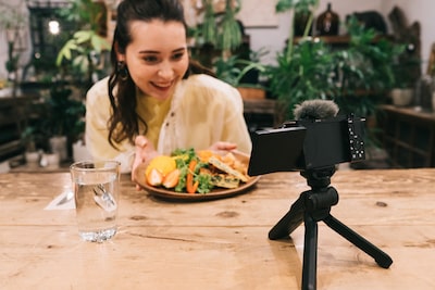 Imagen de una mujer sentada con alimentos en una mesa y mirando a la cámara colocada sobre un pequeño trípode