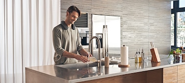 Hombre lavando platos en la cocina mientras escucha música con un parlante portátil SRS-NS7